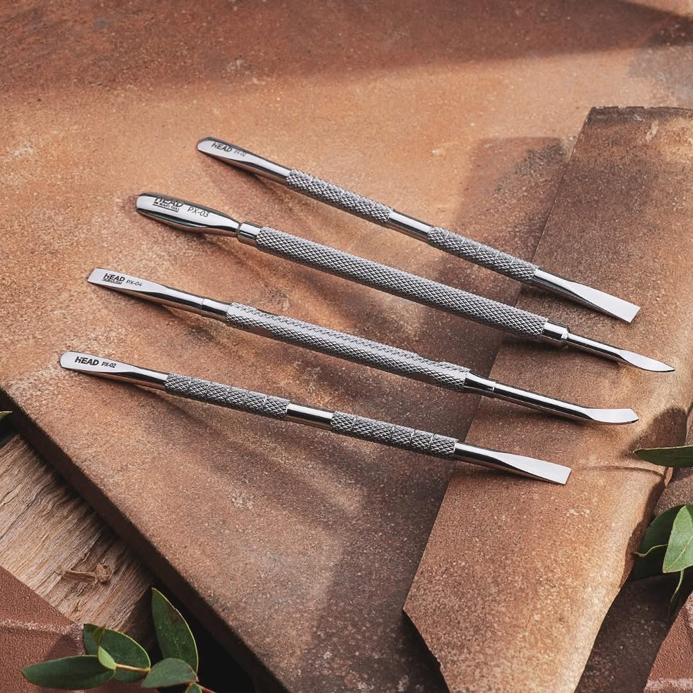 Set of silver professional stainless steel cuticle pusher with a textured handle and a polished working end instruments on a brown surface with green leaves.